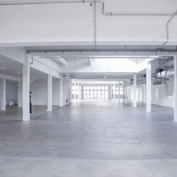 Große, leere, helle Lagerhalle mit weißen Wänden und Betonboden.