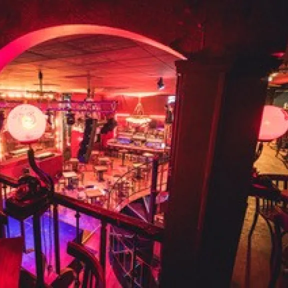 Bar mit rötlicher Beleuchtung, leeren Tischen und festlicher Atmosphäre.