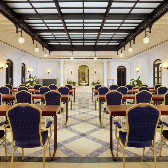 Eleganter Konferenzraum mit Reihen blauer Stühle und Tischen, hohe Decke, helle Beleuchtung.