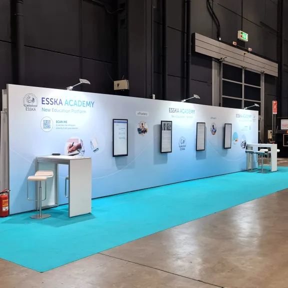 Messestand mit weißer Wand, Bildschirmen und blauem Teppich.