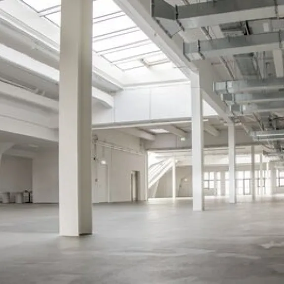Große, helle Halle mit weißen Wänden und Fenstern im Dach, industrieller Stil.