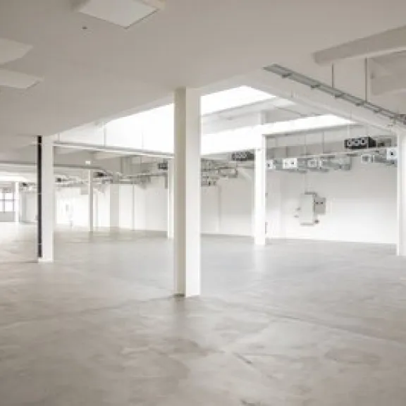 Leere, helle Industriehalle mit weißen Wänden und Betonboden.