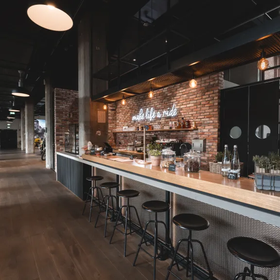 Moderne Cafétheke mit hohen Hockern, Backsteinwand und warmem Licht.