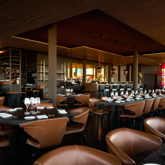 Modernes Restaurant mit braunen Ledersesseln und gedeckten Tischen, warm beleuchtet.
