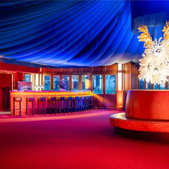 Elegante Bar mit leuchtenden Farben, blauer Decke und großer weißer Skulptur im Zentrum.