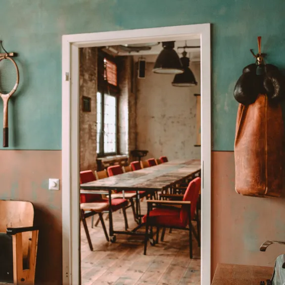 Tisch mit roten Stühlen in einem vintage Raum, Boxsack und Tennisschläger an der Wand.