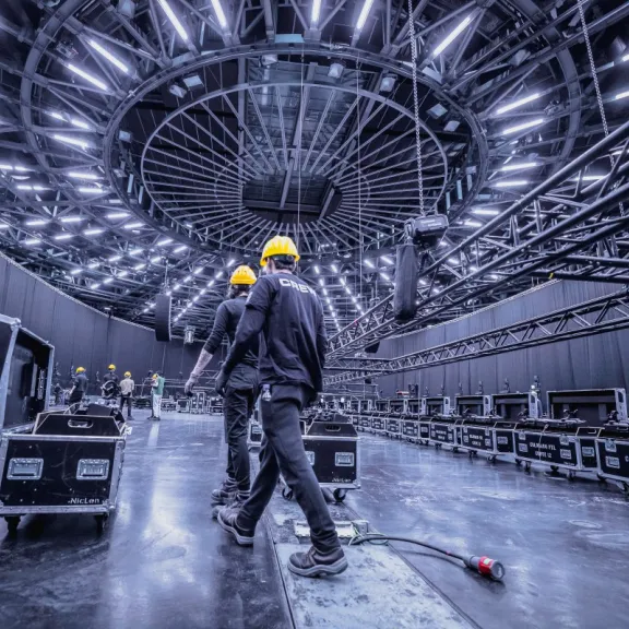 Zwei Arbeiter mit gelben Helmen unter einer futuristischen, beleuchteten Decke in einer Halle.