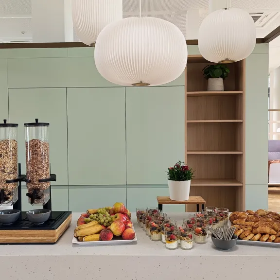 Frühstücksbuffet mit Müsli, Obst, Gebäck und großen runden Lampen darüber.