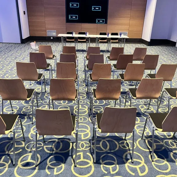 Leerer Konferenzraum mit Reihen von Stühlen und einem Tisch vorne.