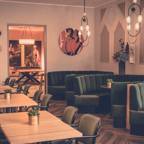 Gemütliches Café mit grünen Polsterbänken, Holztischen und moderner Wanddekoration.