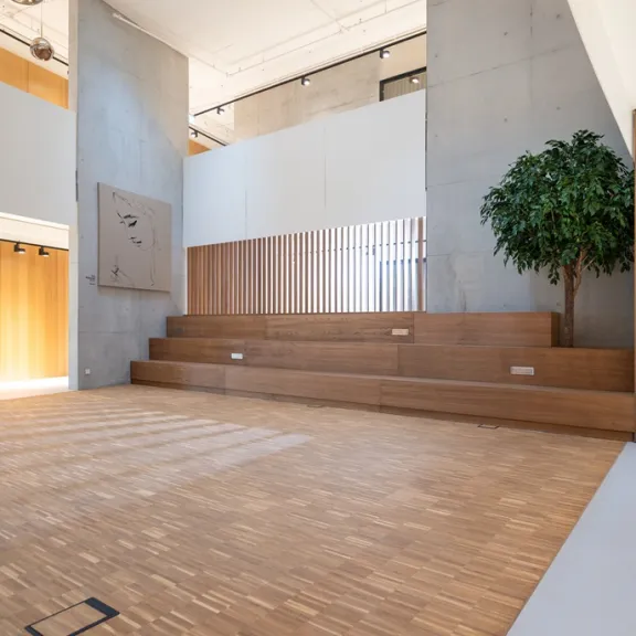 Helles, modernes Atrium mit Holzstufen und großem grünen Baum.