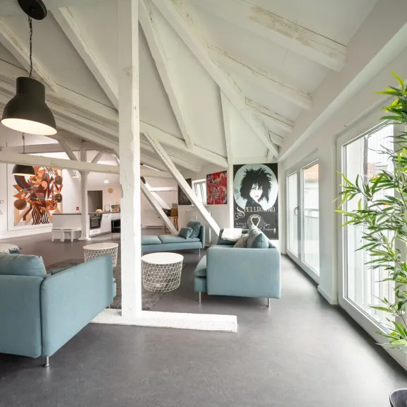 Modernes Loft mit blauen Sofas, großen Fenstern, Kunstwerken und einer grünen Pflanze.