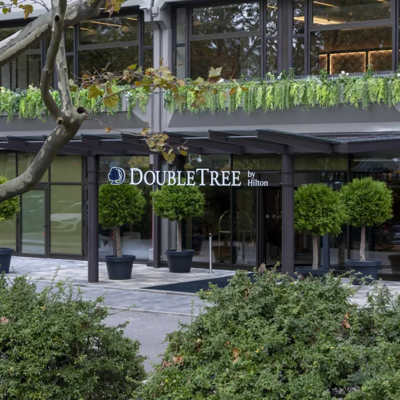 Hoteleingang von DoubleTree mit Glasfassade und grünen Pflanzen in Töpfen.