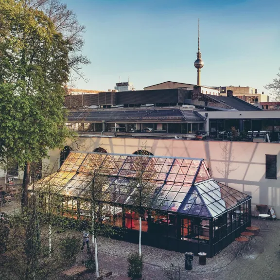 Glaspalast, Sitzbänke und Fernsehturm im Hintergrund bei klarer Himmel.