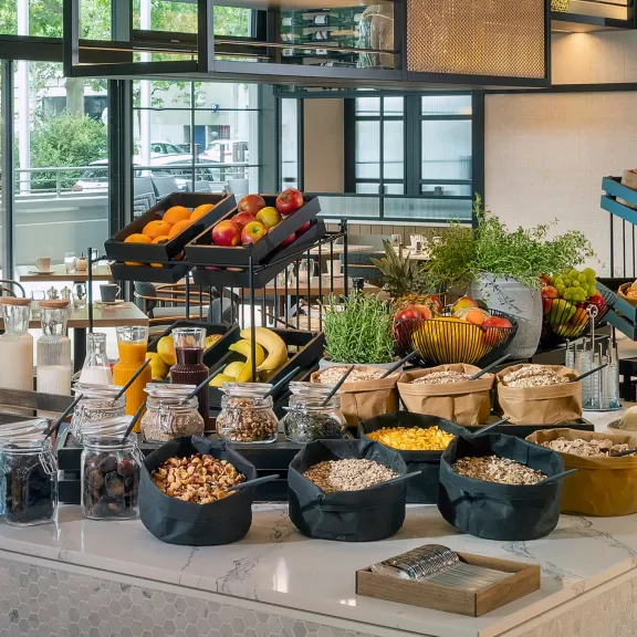 Frühstücksbuffet mit frischem Obst, Brot, Müsli, Marmelade und Säften in modernem Restaurant.