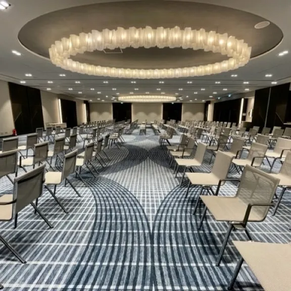 Konferenzraum mit vielen leeren Stühlen und großem, rundem Kronleuchter.
