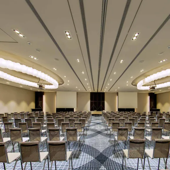 Großer, leerer Konferenzraum mit vielen aufgereihten Stühlen und moderner Beleuchtung.