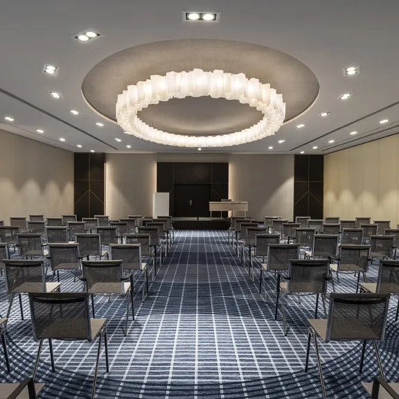 Konferenzraum mit leeren Stuhlreihen, Teppichboden und großem Rundlicht an der Decke.
