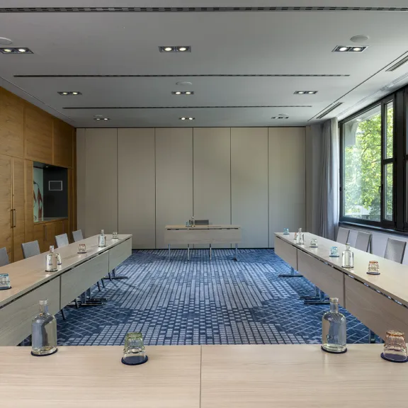 Moderner Konferenzraum mit U-förmigem Tisch, Wassergläsern und großen Fenstern.