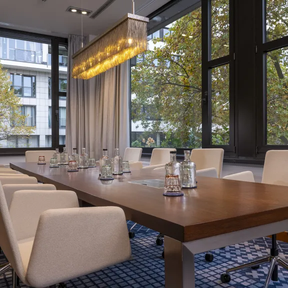 Moderner Konferenzraum mit großem Holztisch, weißen Stühlen und großen Fenstern.