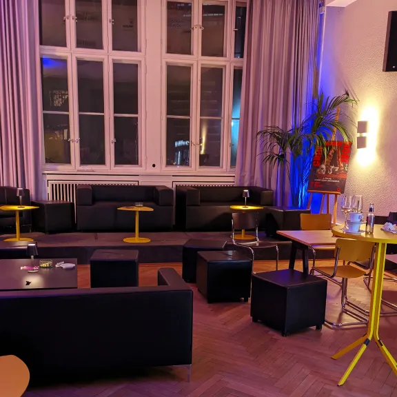 Gemütliche Lounge mit schwarzen Sofas, gelben Tischen und stimmungsvollem Licht.