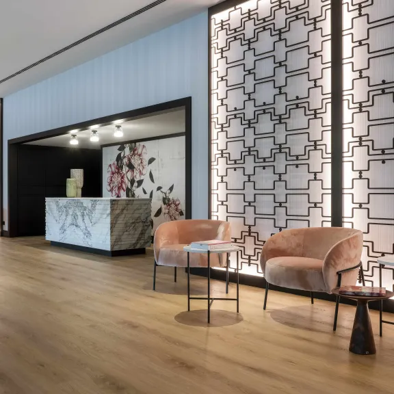 Heller Hotellobby mit modernen Sesseln und Empfangstresen, Holzboden und Designwänden.