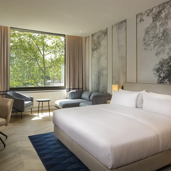 Modernes Hotelzimmer mit Doppelbett, großem Fenster und gemütlicher Sitzecke.