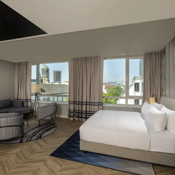Modernes Hotelzimmer mit Doppelbett, Sitzbereich und großen Fenstern mit Stadtblick.