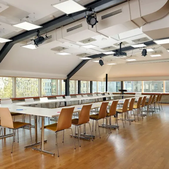 Moderner Konferenzraum mit langen Tischen, Holzstühlen und großen Fenstern