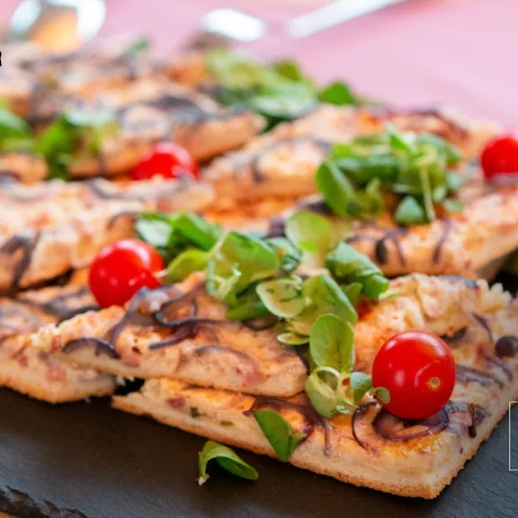 Rechteckige Flammkuchentücke mit Rucola und Kirschtomaten auf einer Schieferplatte.