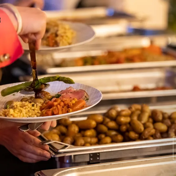 Person nimmt Essen vom Buffet, verschiedene warme Speisen auf Tellern