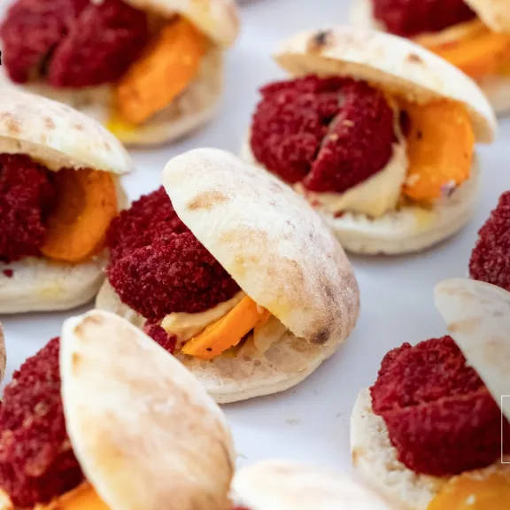 Mini-Pita-Brötchen mit Falafel und orangefarbenem Gemüse auf weißem Teller.