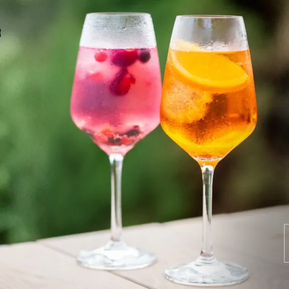 Zwei Gläser mit bunten Sommerdrinks, eines mit Beeren, eines mit Orangenscheiben.