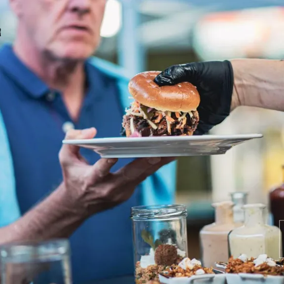 Mann erhält einen Burger auf einem weißen Teller an einem Foodtruck.
