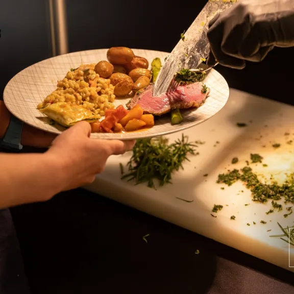 Eine Person erhält auf einem Teller Fleisch und Beilagen an einer Buffetausgabe.
