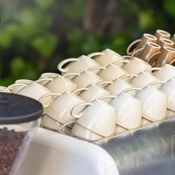 Reihe gestapelter Kaffeetassen auf einer Espressomaschine, daneben Kaffeebohnenbehälter.