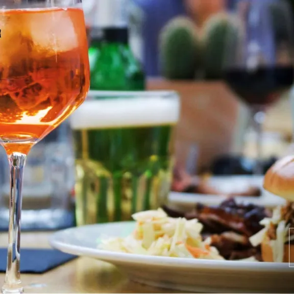 Burger mit Cole Slaw, Bier und Aperol Spritz auf einem Restauranttisch.