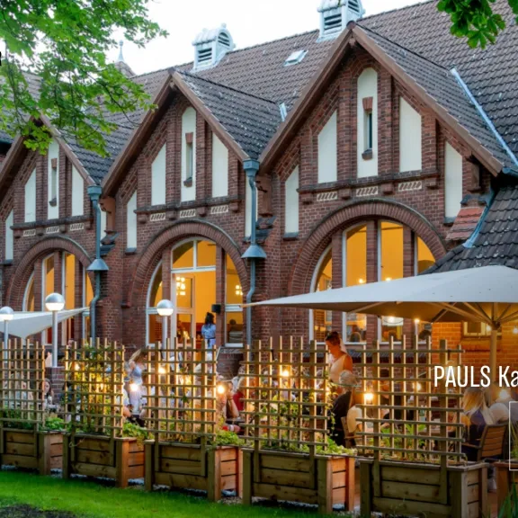 Gemütlicher Locationgarten vor einem Backsteinhaus mit Lichterketten und Holzzaun.