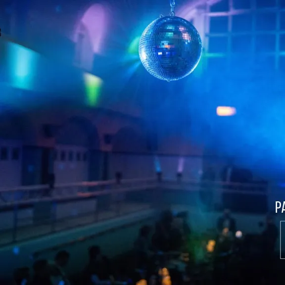 Disco-Kugel unter buntem Licht in einem Club mit tanzenden Menschen.