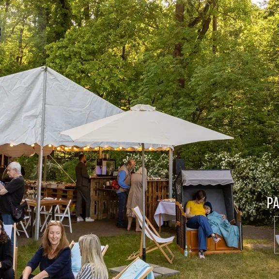 Gartenfest mit weißen Zelten, Menschen plaudern entspannt im Grünen.