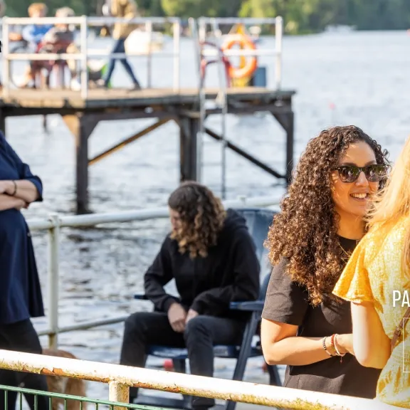 Mehrere Personen unterhalten sich entspannt am Seeufer bei sonnigem Wetter.