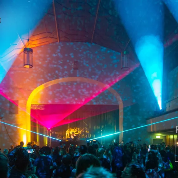 Bunte Lichter und Laser auf einer vollen Festivalbühne in einer Halle.