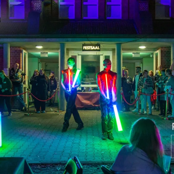 Zwei Künstler jonglieren mit leuchtenden Stäben vor Publikum bei Nacht.