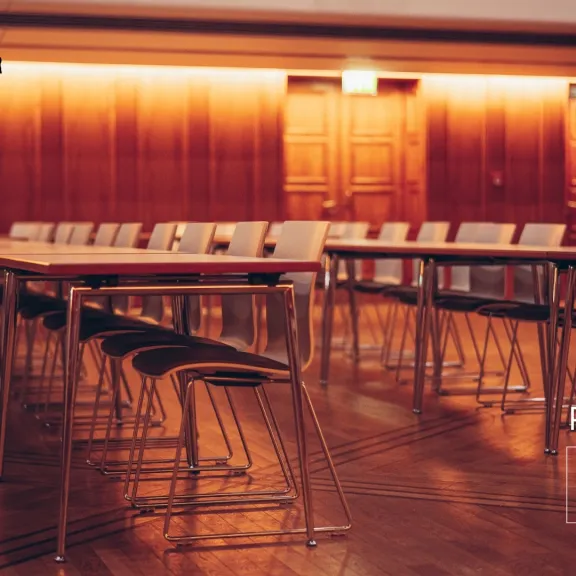 Leerer Konferenzraum mit aufgereihten Stühlen und Tischen, warm beleuchtet.