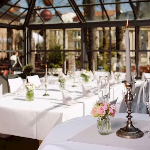 Festlich gedeckter Tisch im Wintergarten mit Kerzenständern und Blumen.