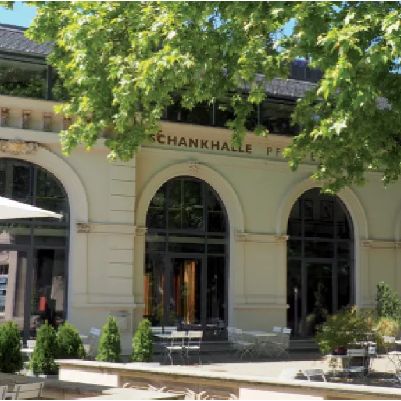 Schankhalle Pfefferberg mit großen Fenstern, Sitzplätzen im Freien und Bäumen im Sonnenschein.