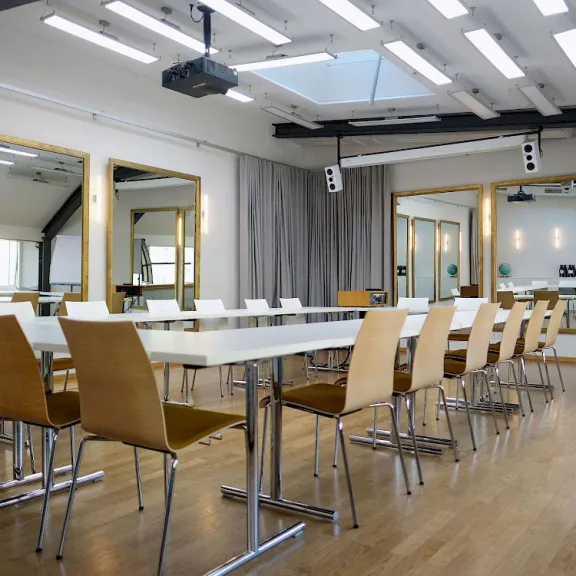 Moderner Konferenzraum mit langen Tischen, Holzstühlen und großen Spiegeln an den Wänden.
