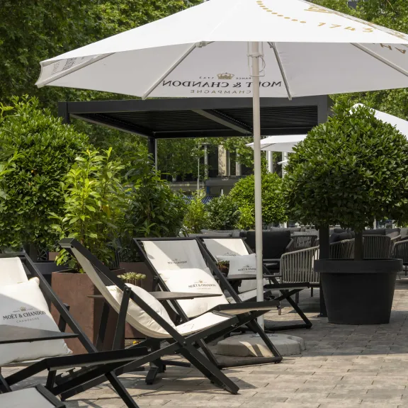 Liegestühle und Sonnenschirme auf einer sonnigen Terrasse mit grünen Pflanzen.