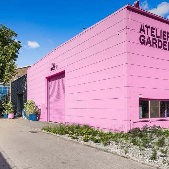 Pinkes Gebäude mit der Aufschrift "Atelier Gardens" an einem sonnigen Tag.