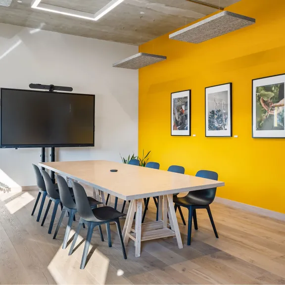 Moderner Besprechungsraum mit gelber Wand, großem Bildschirm und Kunstwerken an der Wand.